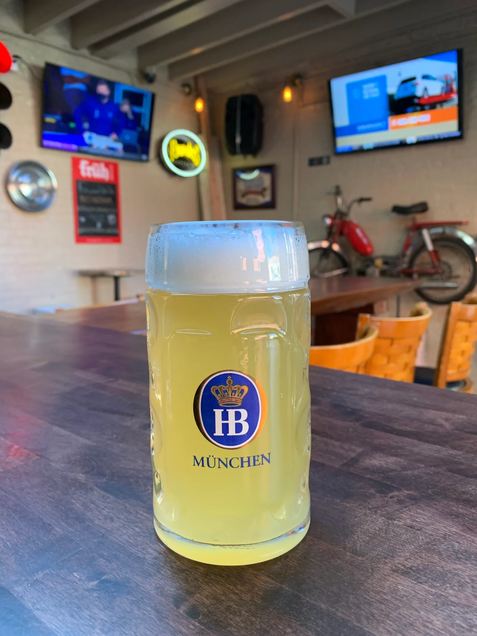 A glass of beer on the bar at The Beer Garage in Park Slope with two wall-mounted televisions behind it, a place to watch NBA in Brooklyn